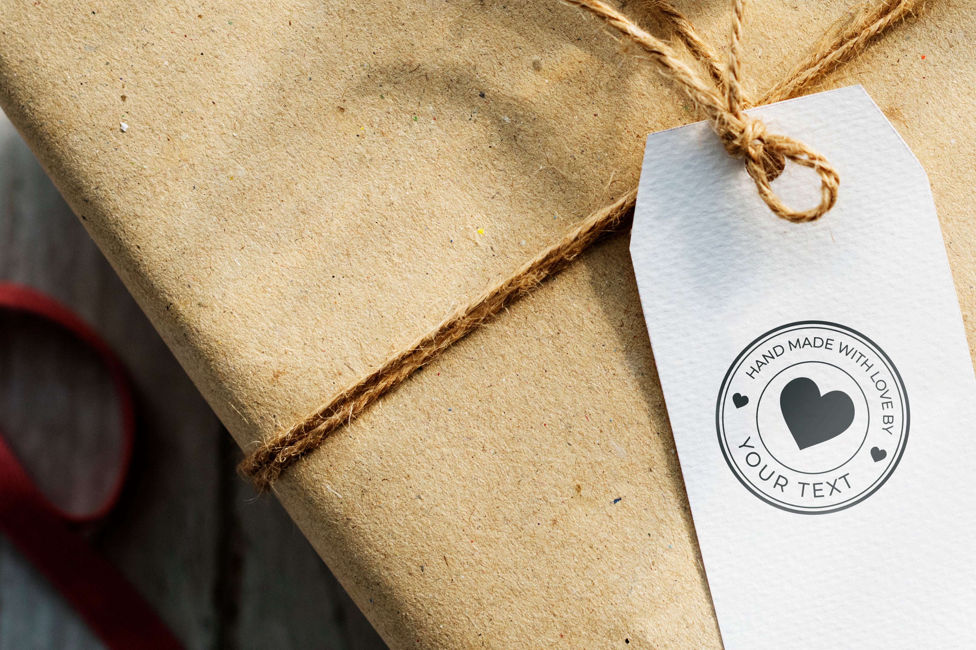 Custom stamp on a gift tag that says 'Hand Made with Love by Your Text,' attached to a brown wrapped package.