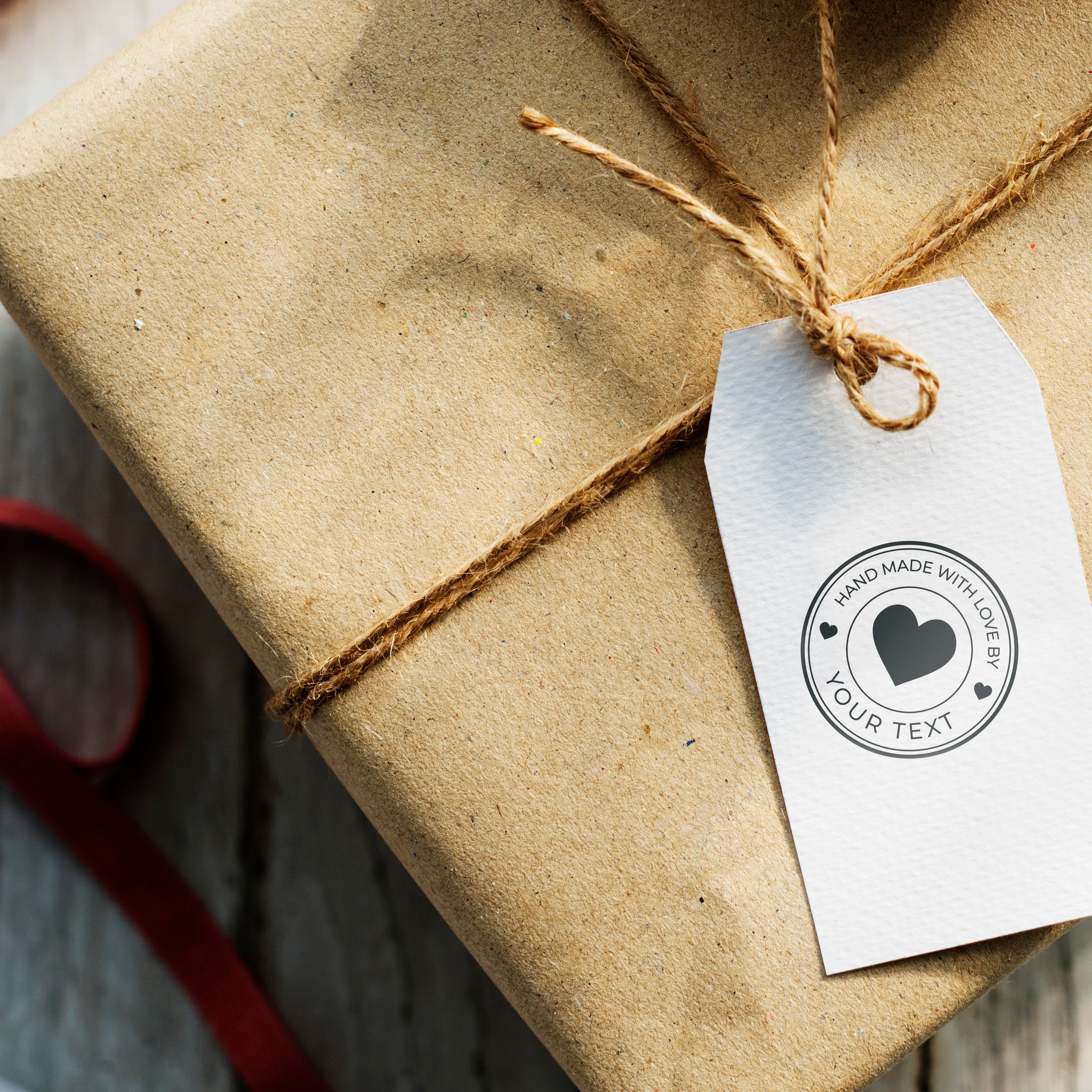 Custom stamp on a gift tag that says 'Hand Made with Love by Your Text,' attached to a brown wrapped package.