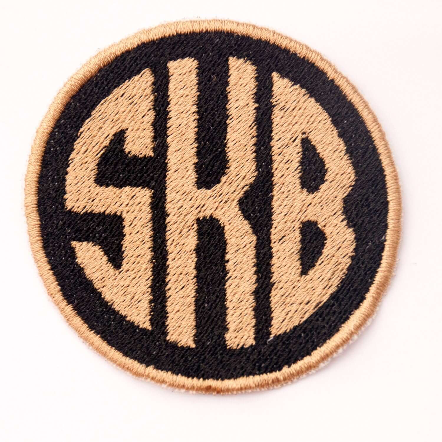 Custom embroidered monogram patch with the initials SKB in a circular design on a black background.