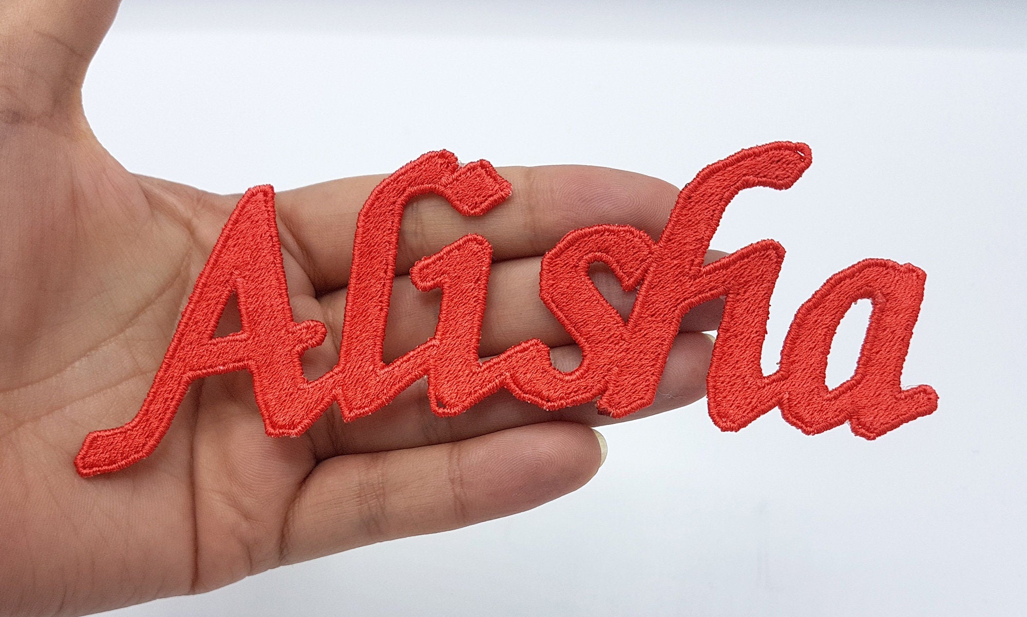 Personalized red embroidered name patch 'Alisha' held in hand, ideal for swimwear and sportswear.