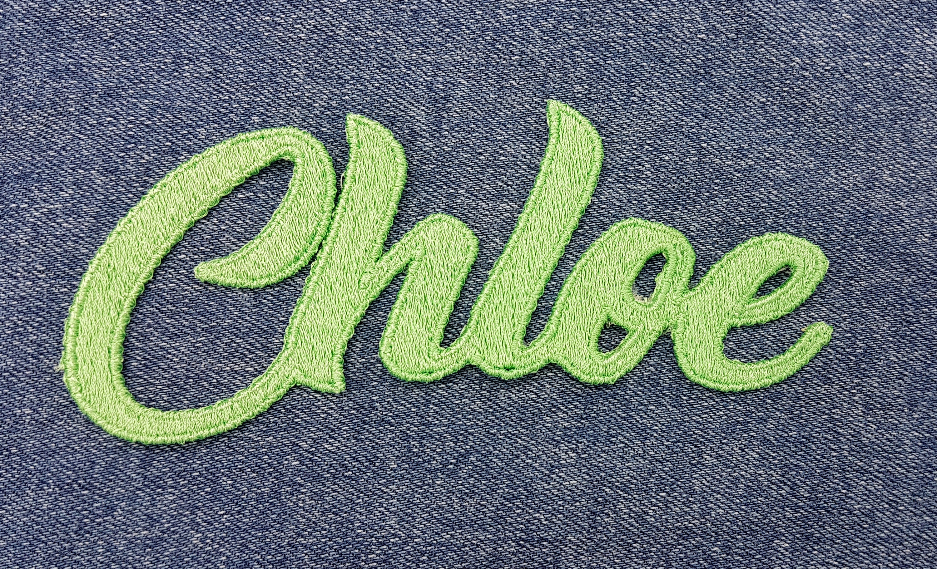 Embroidered name patch 'Chloe' in vibrant green on denim background, featuring 100% embroidery.