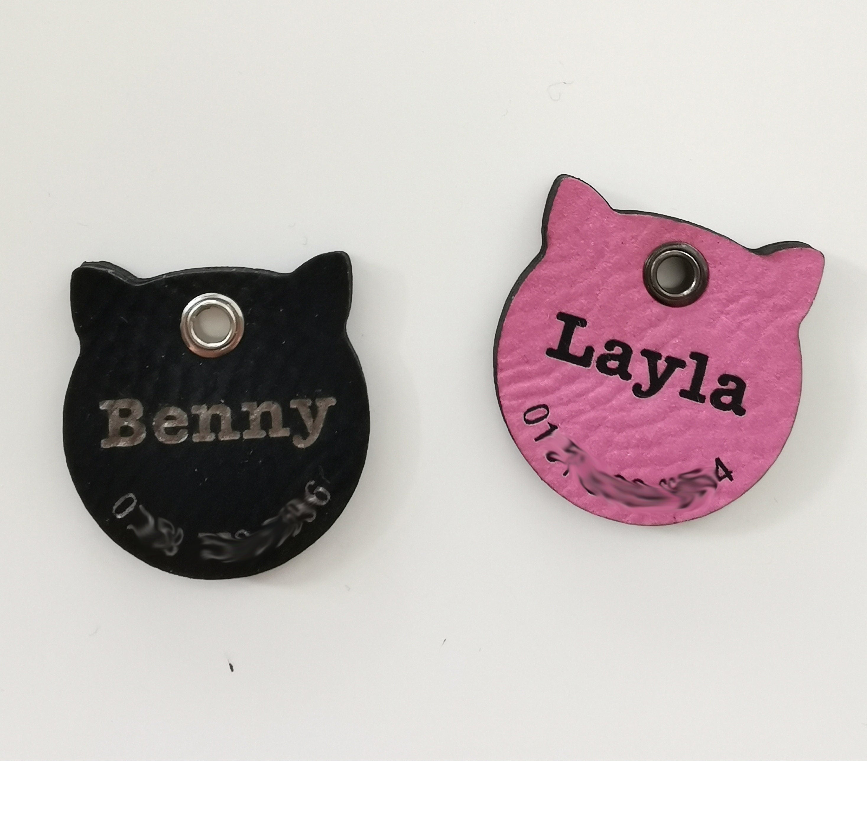 Custom leather cat name tags in black and pink, laser engraved with names Benny and Layla.