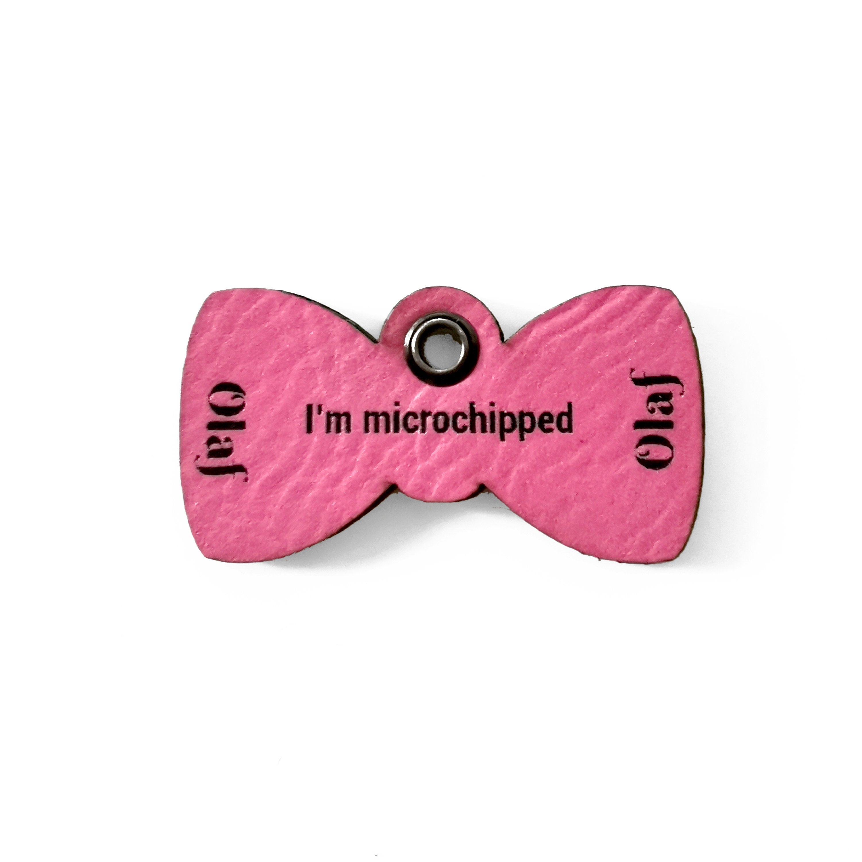 Custom pink leather cat name tag with bow tie design, reading 'Olaf' and 'I'm microchipped'.