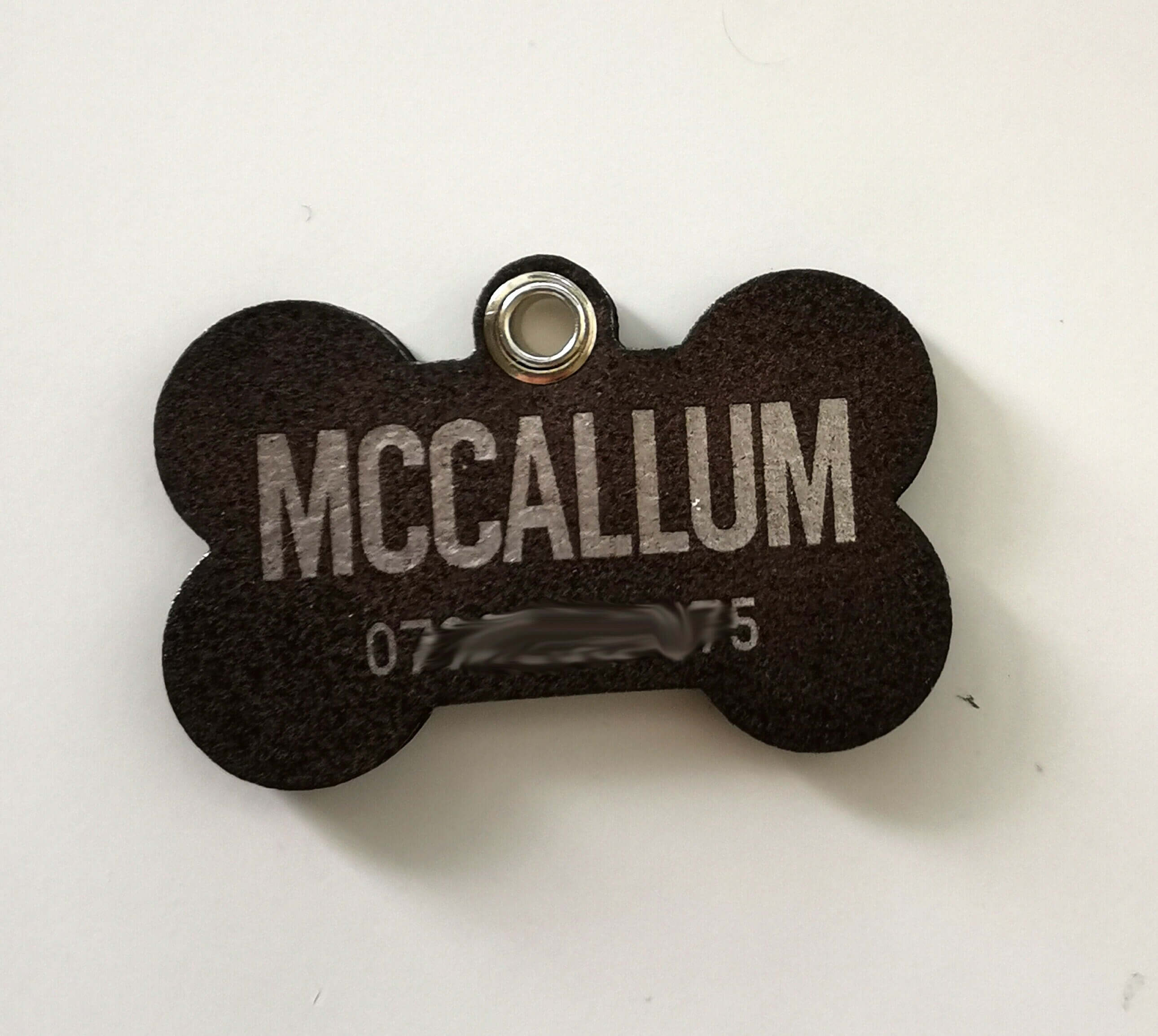 Custom engraved leather dog name tag in bone shape with the name McCallum and a stainless-steel ring.