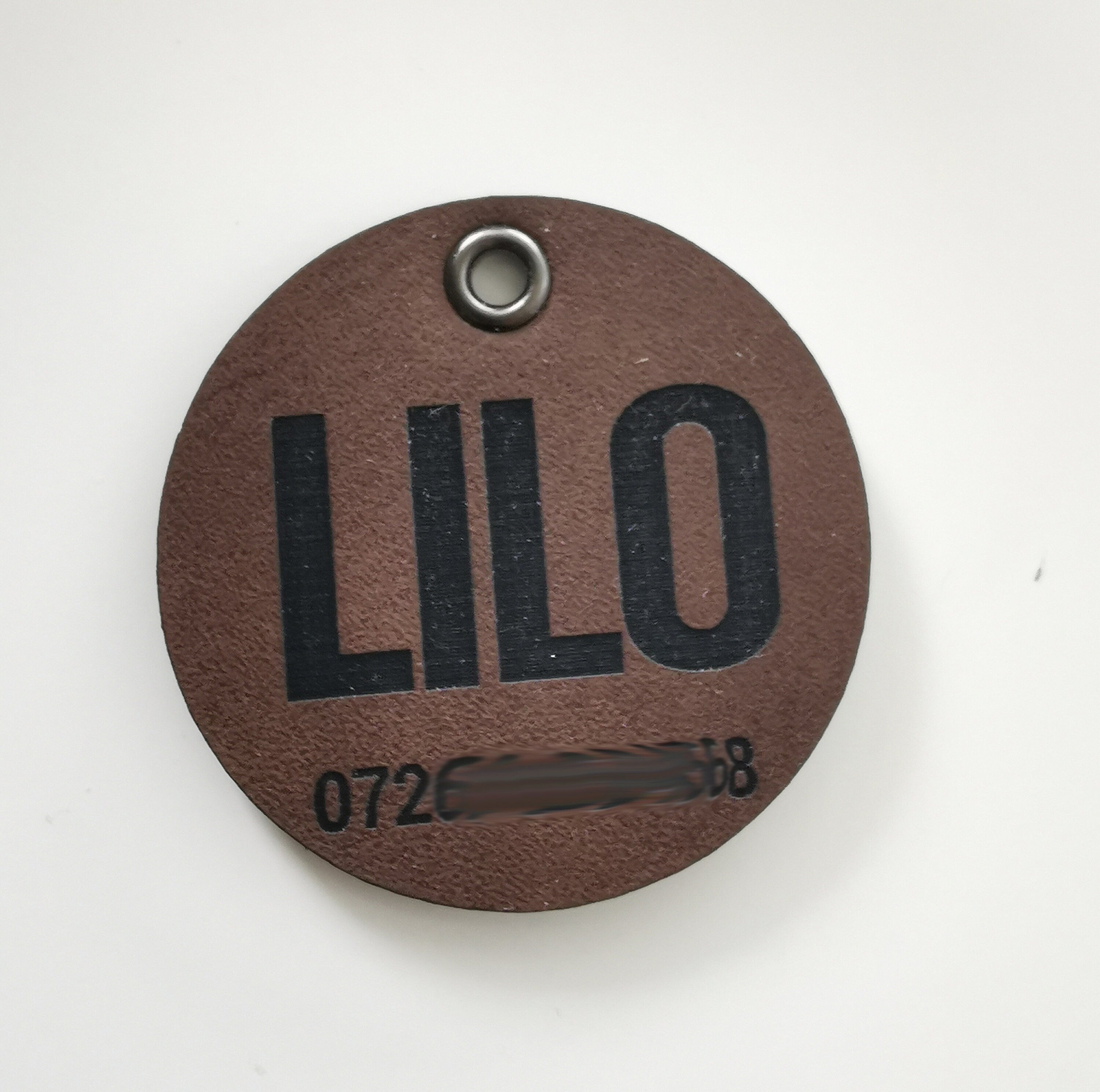 Custom brown leather dog name tag with engraved text 'LILO' and ID number, personalized pet accessory.