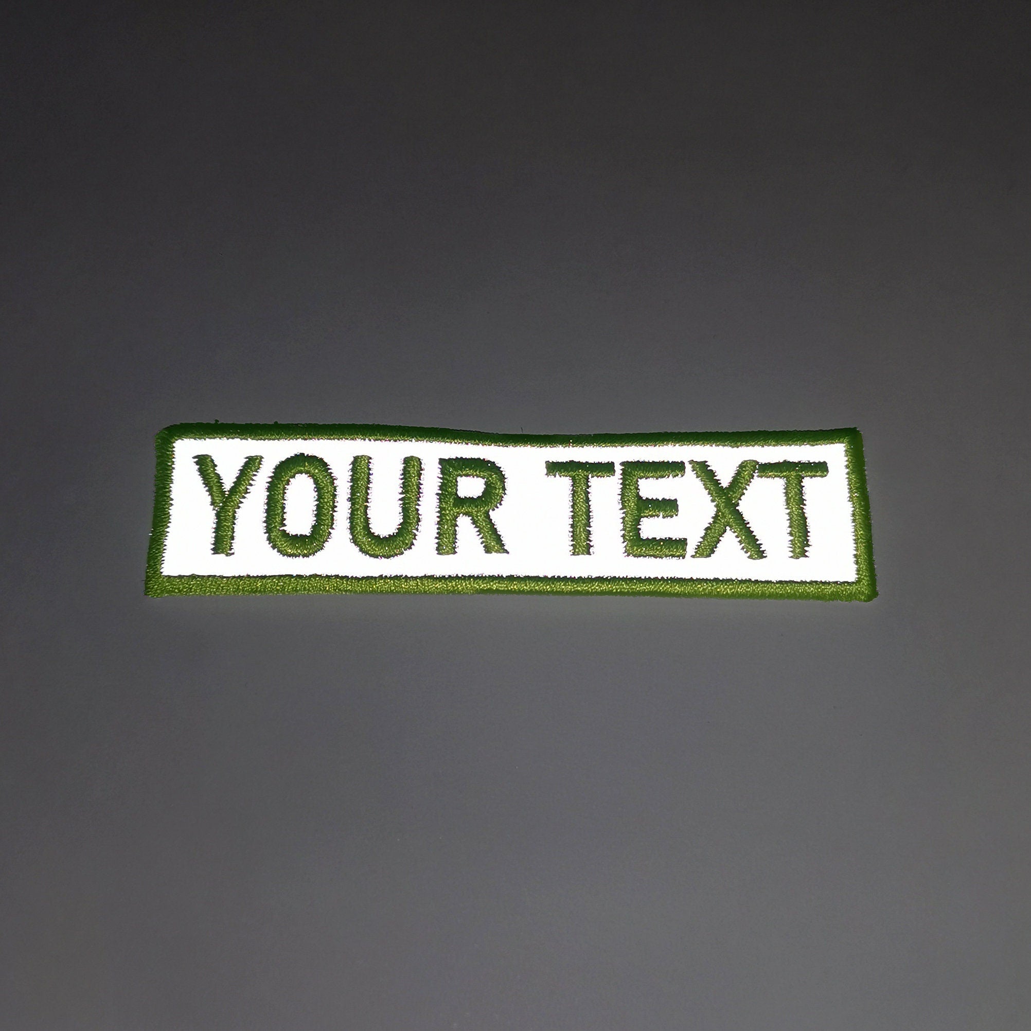 Custom reflective name patch with green border and white embroidery showing 'YOUR TEXT' for personalized applications.