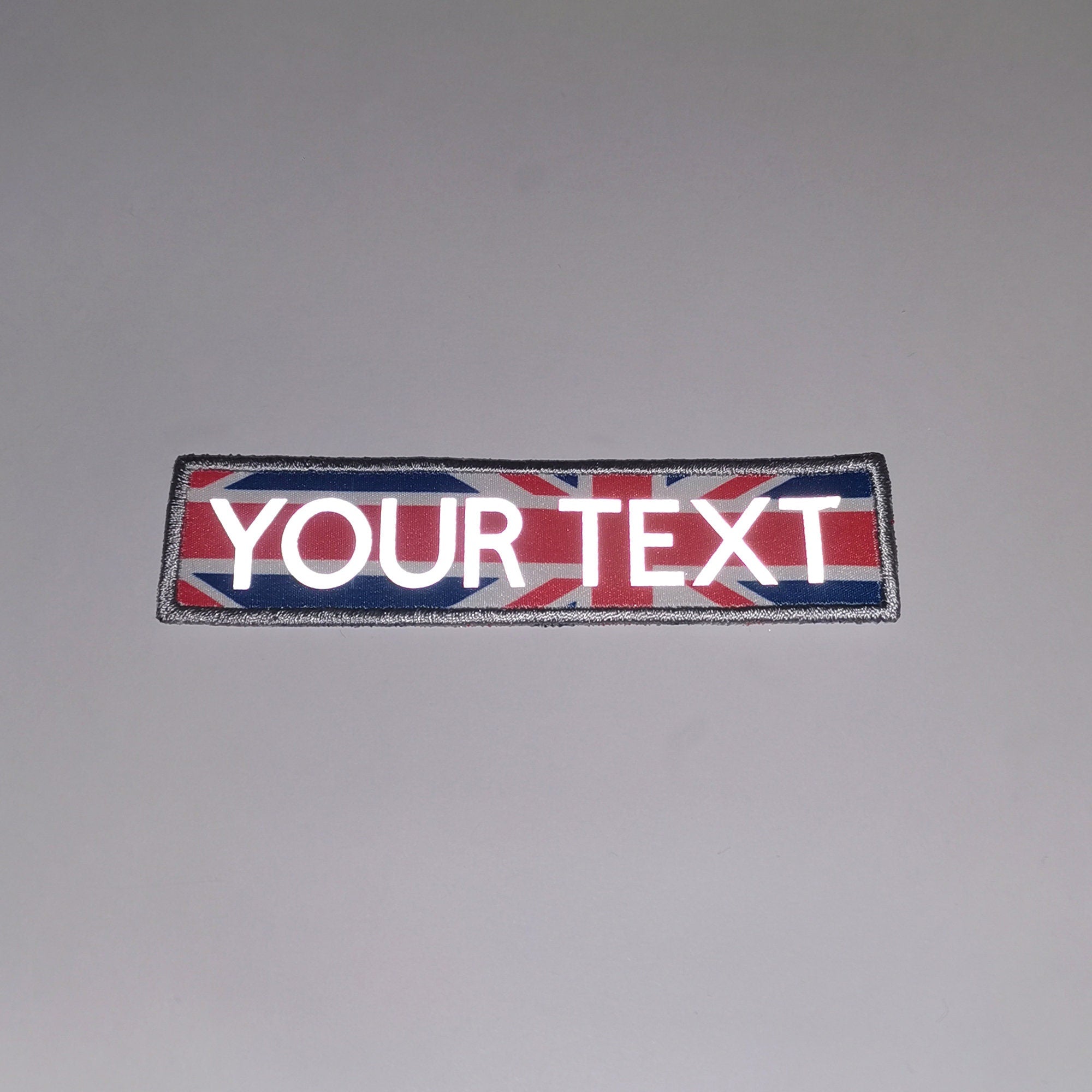 Custom reflective iron on patch with embroidered border and printed letters on a UK flag background.