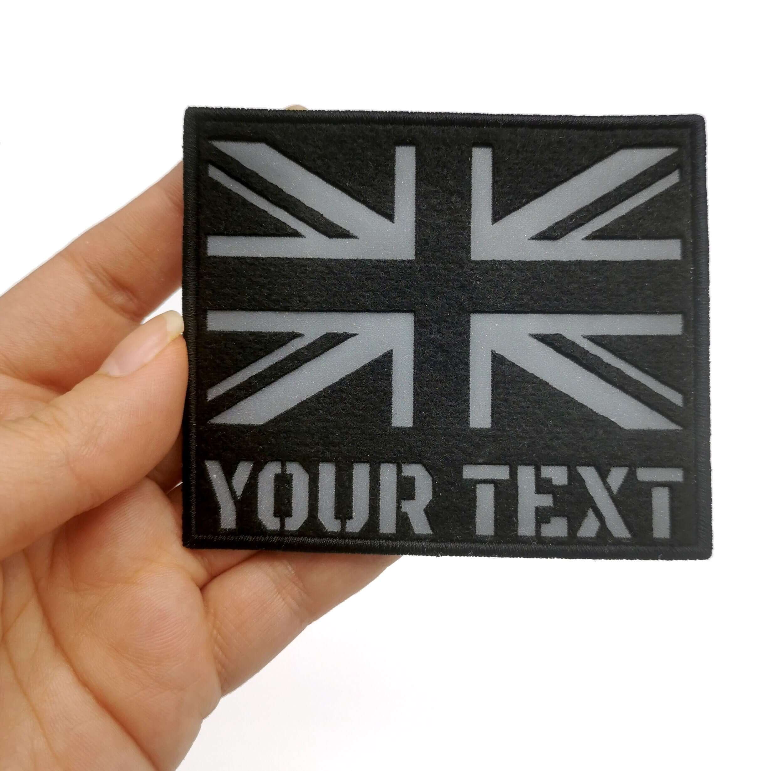 Hand holding a UK reflective flag patch with customizable text, measuring 9x7.3 cm, ideal for military and tactical use.