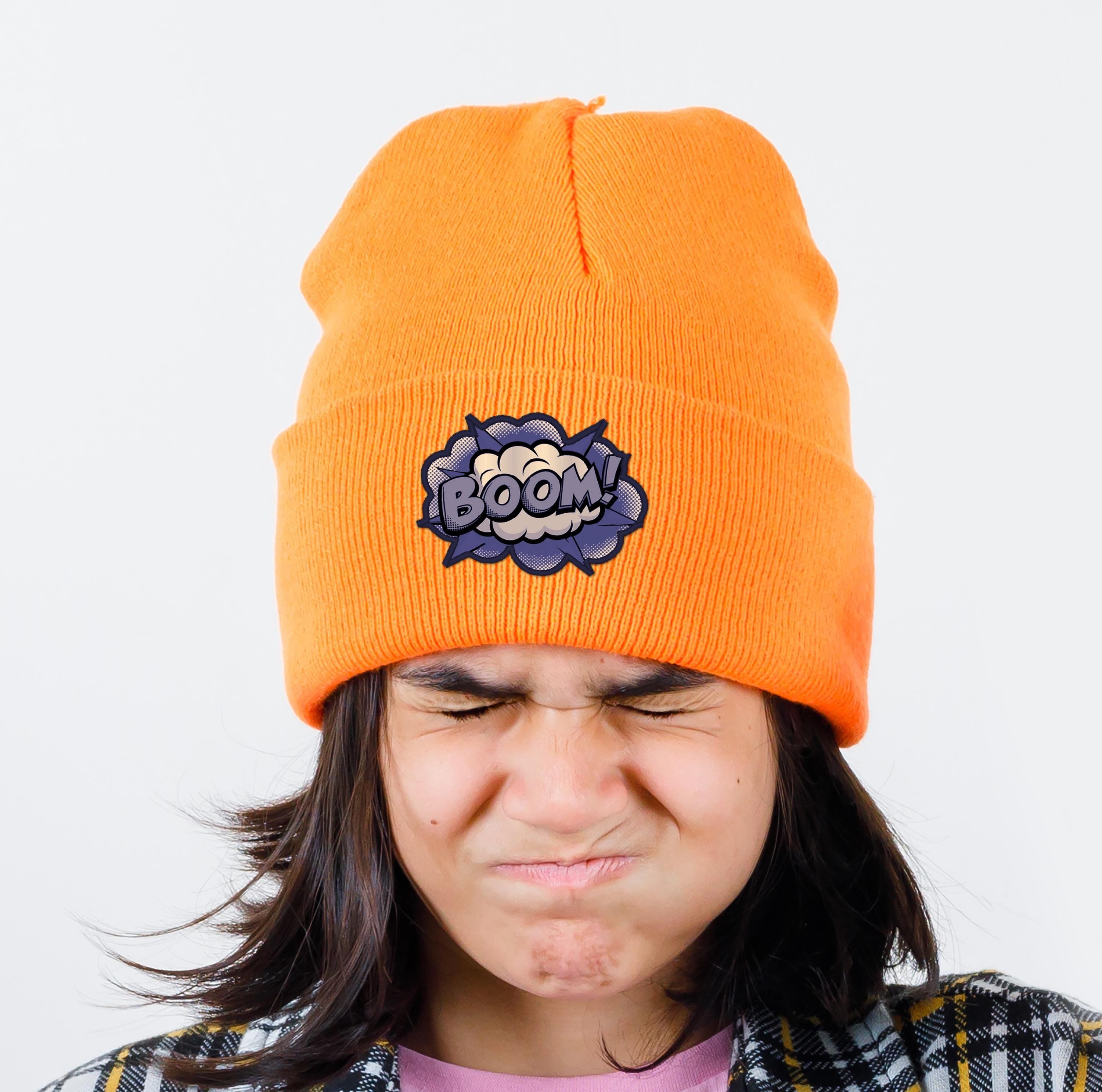 Person wearing an orange beanie with a 'BOOM' patch, showcasing a fun winter accessory.