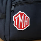 Personalised embroidered monogram patch on a black bag, featuring the initials TMH in vibrant red and white.