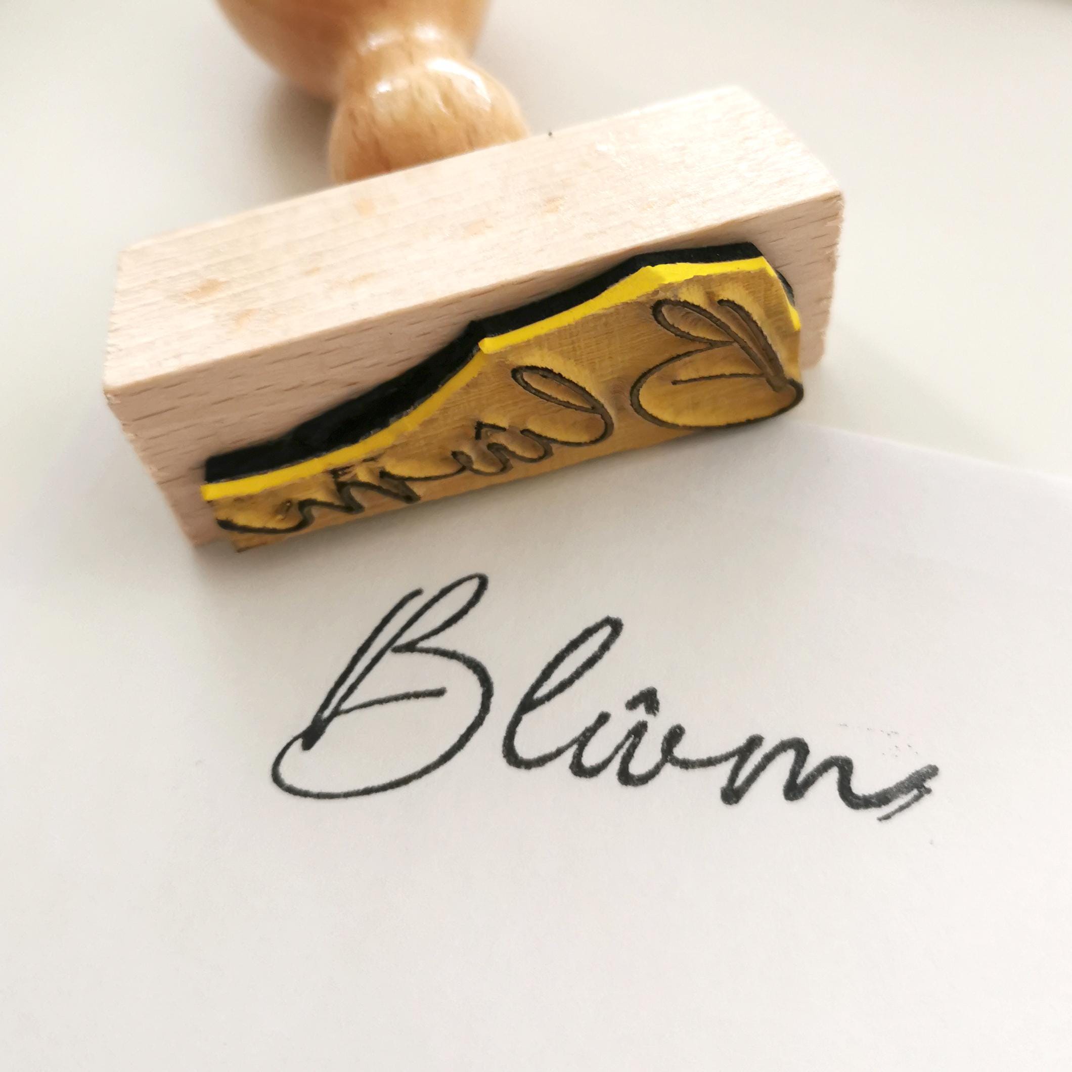 Custom signature stamp with handwritten text 'Blüm' on paper, showcasing personalization for gifts.