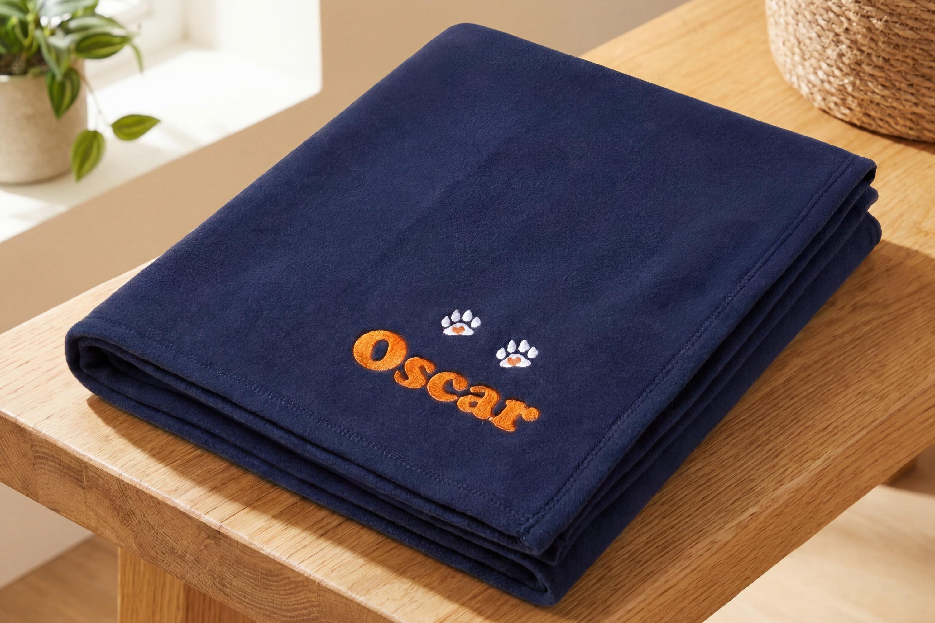 Personalised navy dog blanket with embroidered name and paw prints on oak bench