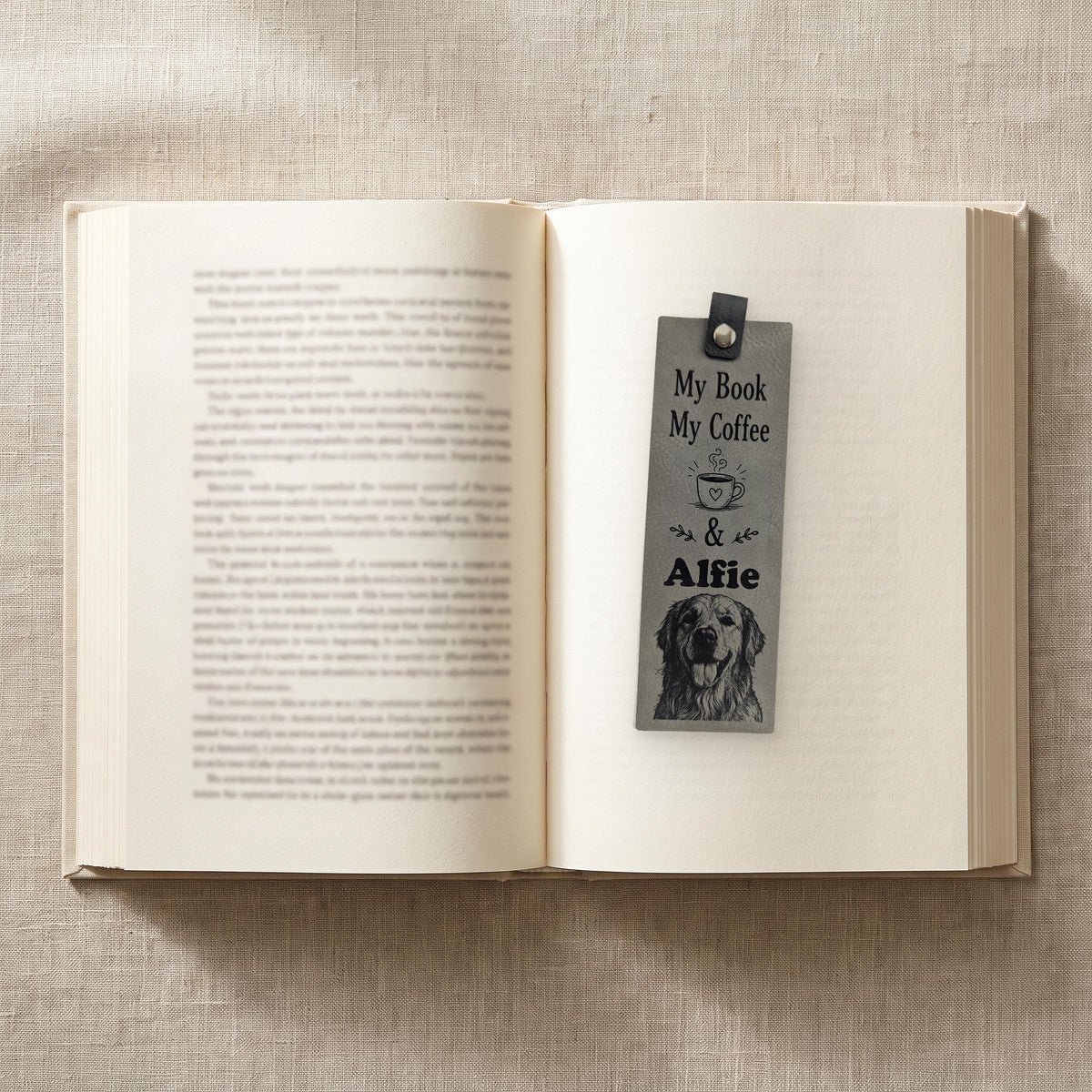 Grey personalised vegan leather bookmark on an open book, engraved with a coffee cup, a pet name and a dog portrait
