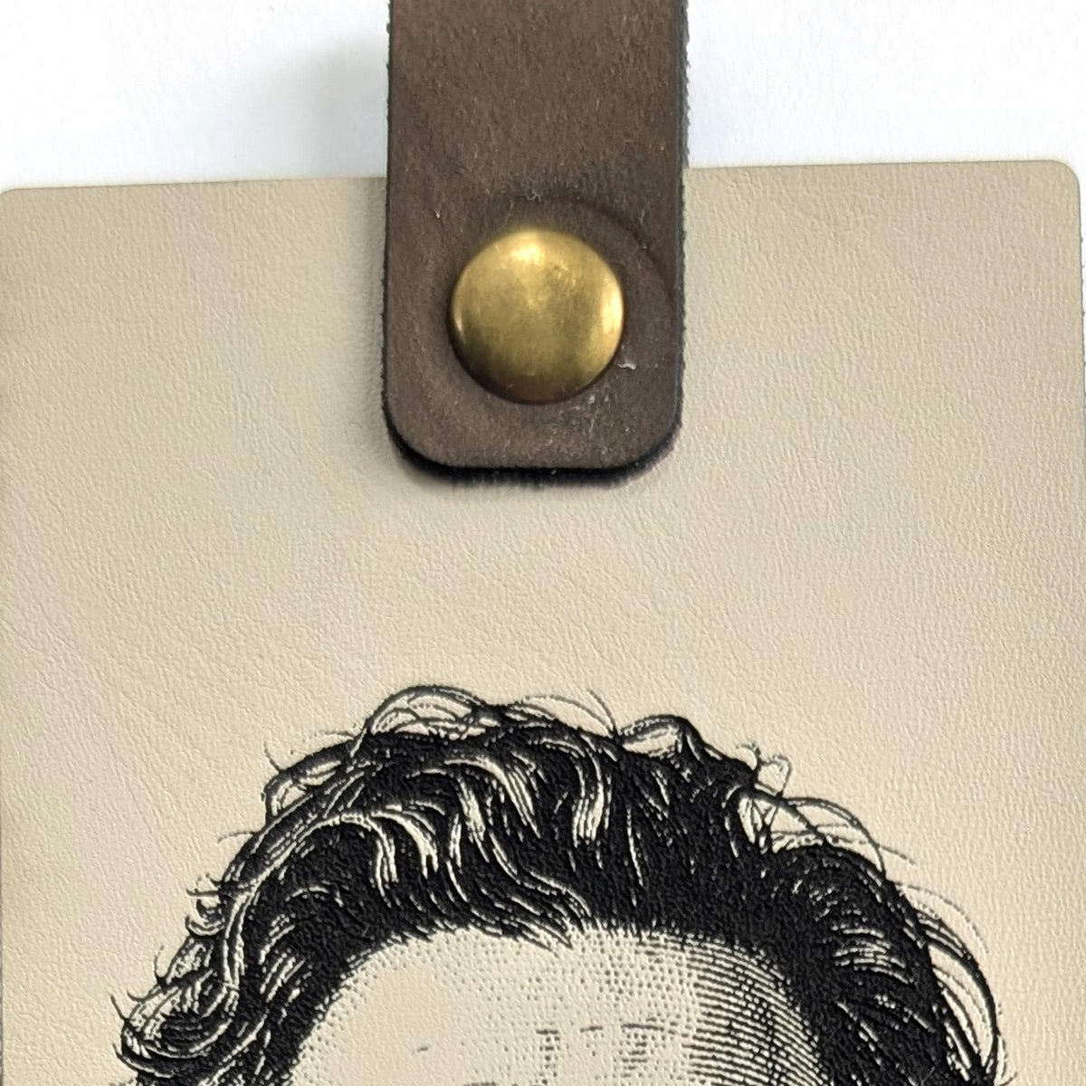 Close-up of the tab and metal snap at the top of the cream vegan leather bookmark