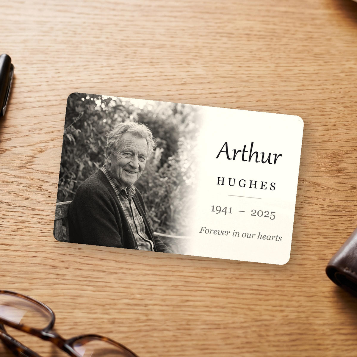 Memorial wallet card on a wooden desk, printed with a black and white photo, a name, years and a short line