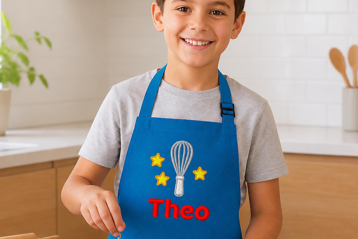 Personalised kids apron in royal blue, embroidered with a whisk, stars and the name Theo