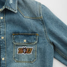Close-up of a denim shirt featuring an embroidered custom patch with the logo 'BU'.