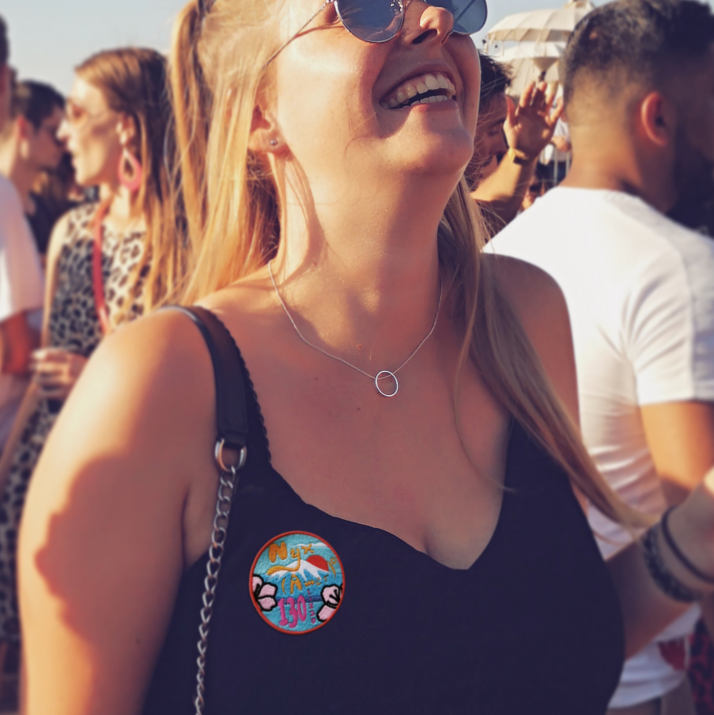 Smiling woman wearing a personalized embroidered patch on her outfit at a lively outdoor event.