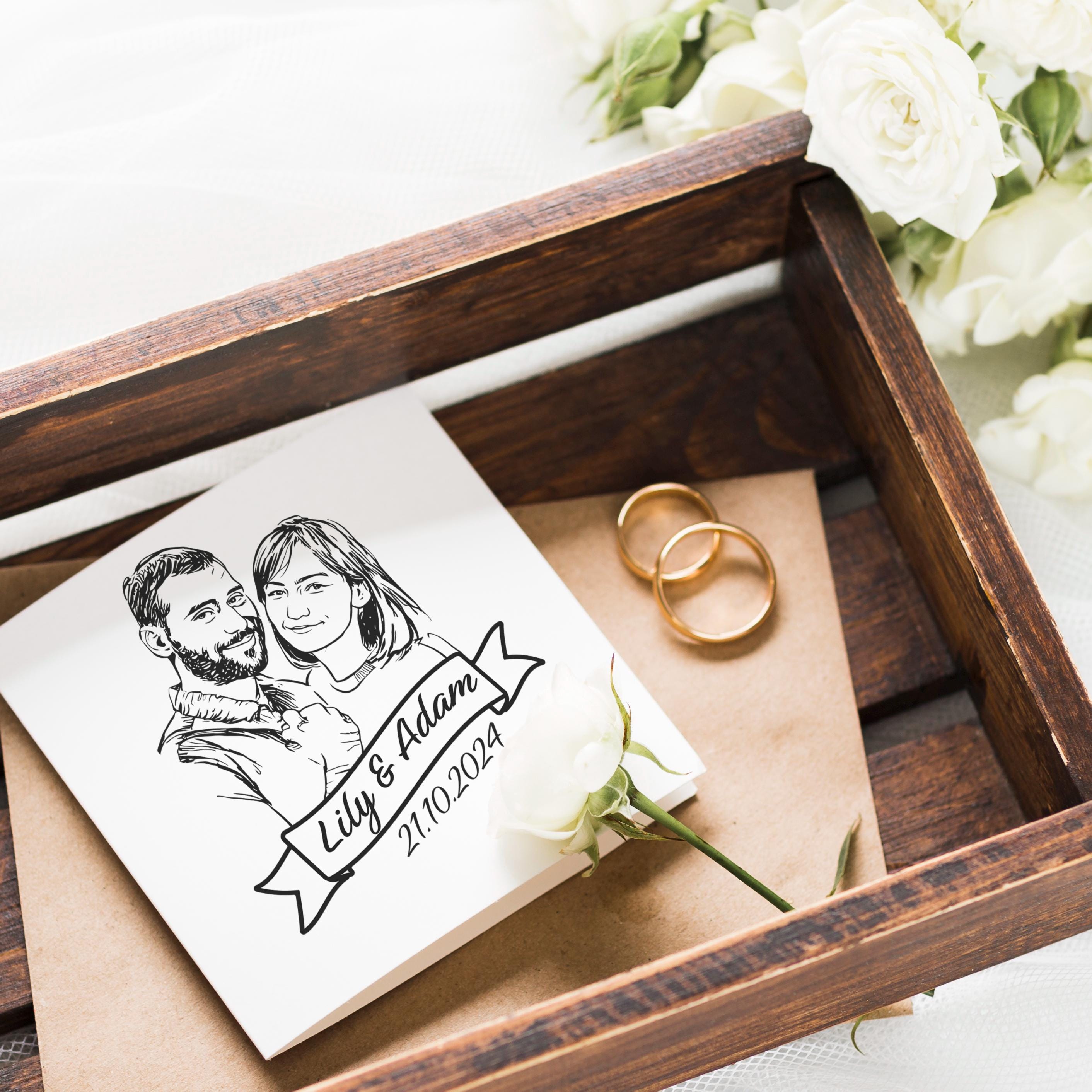 Personalized wedding invitation featuring a couple's illustration, rings, and floral accents in a wooden box.