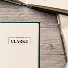 This Book Belongs To personalized stamp on an open book, perfect for book lovers and classrooms.