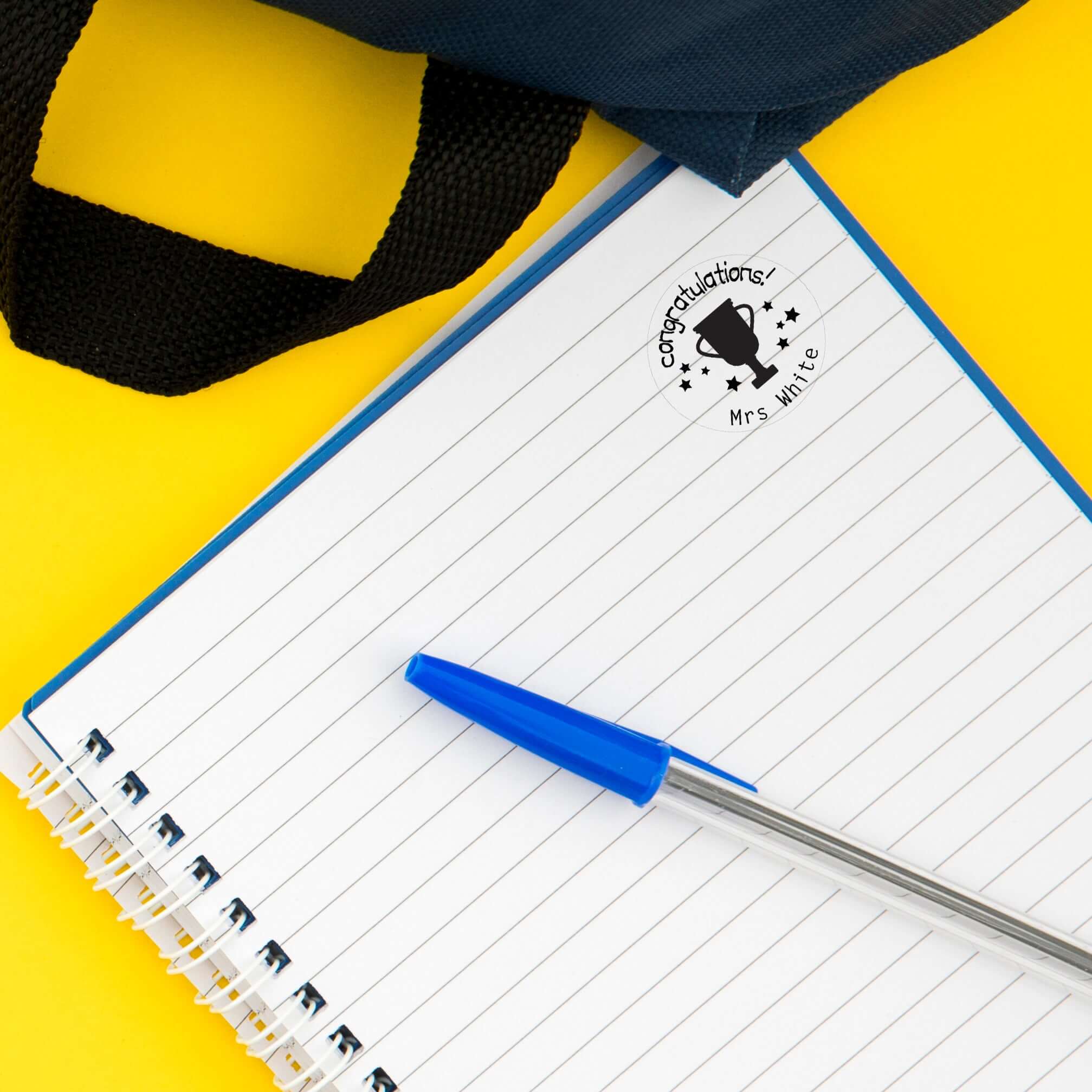 Custom teacher stamp on notebook page with blue pen, perfect for classroom libraries and personalizing gifts.