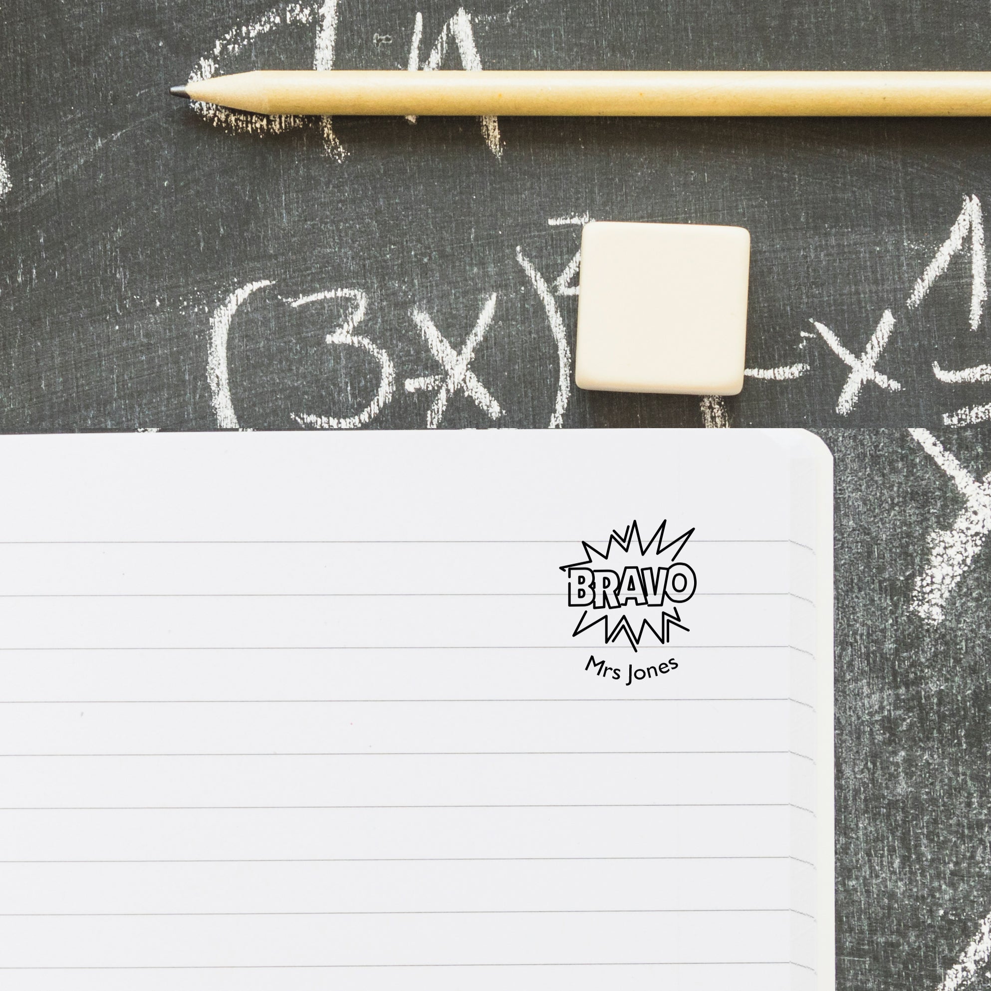 Custom teacher stamp on notebook with pencil, personalized with 'BRAVO' and 'Mrs. Jones' for classroom use.