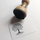 Custom wooden logo stamp with a tree design, used for branding or artwork impressions on paper.