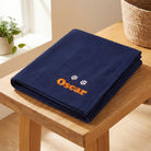 Personalised navy dog blanket with embroidered name and paw prints on oak bench