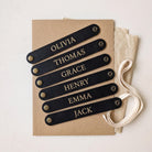 Set of six personalised vegan leather napkin rings engraved with different names, laid flat on kraft card