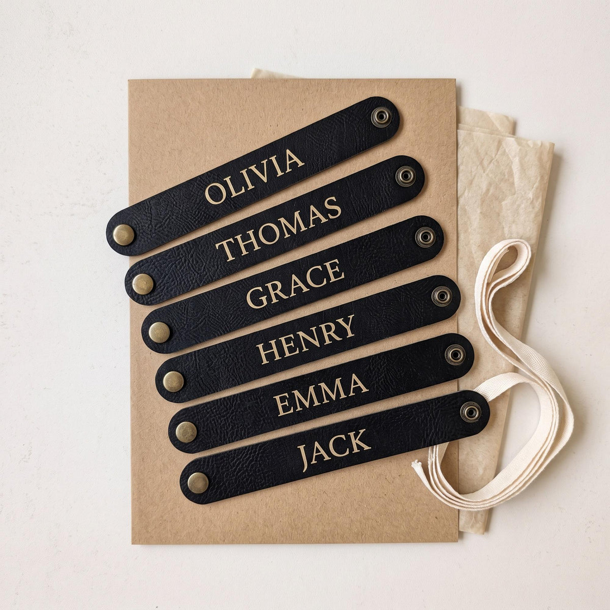 Set of six personalised vegan leather napkin rings engraved with different names, laid flat on kraft card