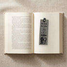 Grey personalised vegan leather bookmark on an open book, engraved with a coffee cup, a pet name and a dog portrait