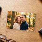 Personalised metal wallet card printed with a couple photo, on a wooden desk beside a wallet and glasses