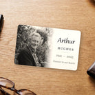 Memorial wallet card on a wooden desk, printed with a black and white photo, a name, years and a short line