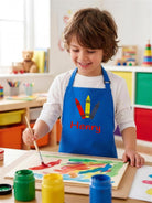 Boy painting in a royal blue kids art apron embroidered with crayons and the name Henry